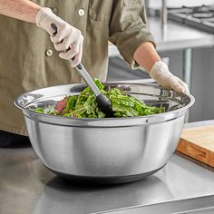 a person in white gloves stirring a bowl with greens