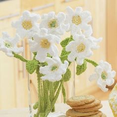 white crocheted flowers in a vase with cookies on the table next to it