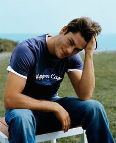 a man sitting on top of a white chair next to the ocean with his head in his hands