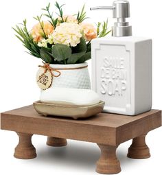 a white soap dispenser sitting on top of a wooden table next to a vase filled with flowers