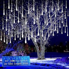 a large tree with lights hanging from it's branches in the middle of a snow covered field