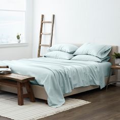 a bed with blue sheets and pillows in a white room next to a wooden ladder