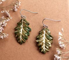 Natural handmade autumn green oak leaf earrings with gold leaf are so much fun to make. As I hand make these stylish vibrant earrings using natural, sustainable local materials the sizes will vary slightly but on average the.. *total drop  is 40-44mm *the pendants are 28-32mm *Made with hypoallergenic elegant stainless steel french earring hooks * Each pair come in a cotton canvas gift bag and I am happy to include a personalised message free of charge. *Free UK shipping and super fast dispatch so you get your order as soon as possible *The backs are un-glazed exposing the wild terracotta coloured clay. Check out my other listings for more unique designs: etsy.mimiwildceramics.com I make all my earrings from clay I forage and process myself from my little cabin in Bristol, UK. Making them Green Leaf-shaped Earrings For Gift, Nature-inspired Hypoallergenic Leaf Earrings, Handmade Leaf-shaped Nature-inspired Earrings, Handmade Leaf-shaped Botanical Jewelry, Oak Leaf Earrings, Canvas Gift Bag, Nature Tree, Green Nature, Oak Leaf