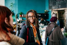 a woman with dreadlocks standing in front of a counter talking to another woman