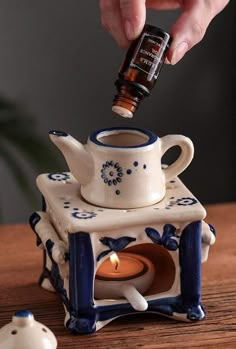 a person is pouring something into a teapot with a candle in it on a table