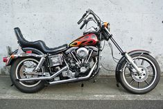 a motorcycle parked next to a wall on the side of the road with flames painted on it