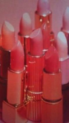 many lipsticks are lined up in rows on a table, one is pink and the other is red