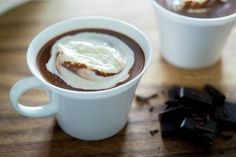 two cups of hot chocolate and marshmallows sit on a table next to each other