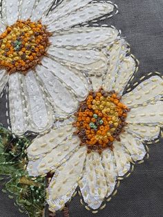 two white flowers with orange centers on a gray background, made out of bead and sequins