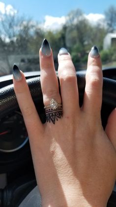 a woman's hand on the steering wheel of a car with her nails painted black