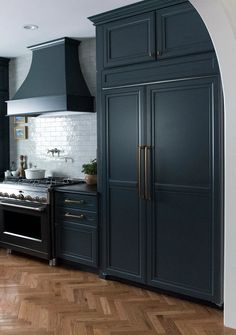 a large kitchen with black cabinets and wood flooring, along with an arched doorway leading to the dining room