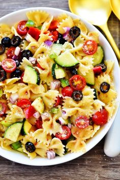 pasta salad with cucumbers, tomatoes and olives in a white bowl on a wooden table