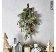 christmas decorations and candles are displayed on a mantel with pine cones, evergreen leaves, and small houses