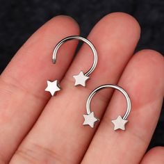 two small silver stars are attached to a pair of nose hoops on someone's finger