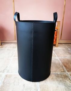 a black leather bucket sitting on top of a tile floor next to a pink wall