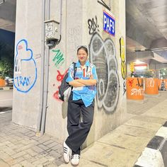 a woman standing next to a wall with graffiti on it's side and her arms crossed