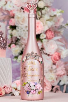 a pink bottle with a tiara on it sitting next to some flowers and cake