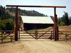 an open gate leading to a barn with mountains in the background