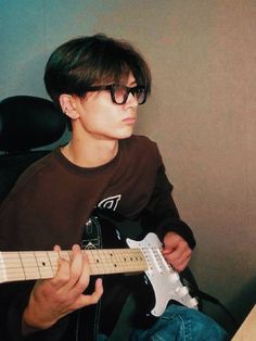 a young man sitting in front of a desk playing an electric guitar while wearing glasses