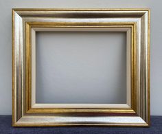 an empty gold frame sitting on top of a blue cloth covered table next to a white wall