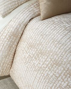 a close up of a bed with white and beige comforter set on top of it