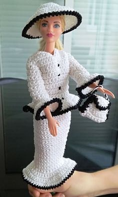 a hand holding a doll wearing a white dress and hat