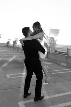 a man holding a woman in his arms while standing on top of a parking lot