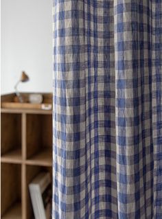 a blue and white checkered curtain hanging in front of a wooden shelf filled with books