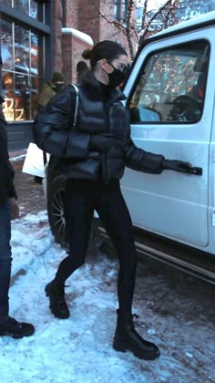 two people standing in the snow next to a white van and one person wearing a face mask