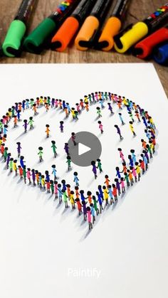 a group of people standing in the shape of a heart surrounded by crayons