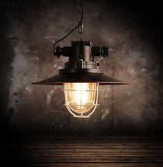 an industrial light hanging from a chain on a wooden floor in front of a dark wall