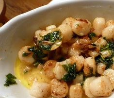 a white bowl filled with shrimp and greens on top of a wooden table next to a fork