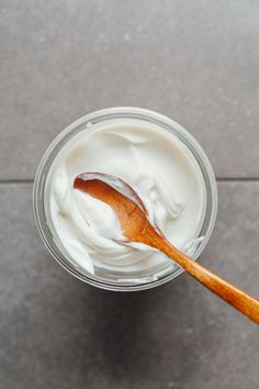 a wooden spoon in a glass jar filled with yogurt on a gray surface