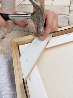 a person holding a hammer and pliers in front of an unfinished piece of wood