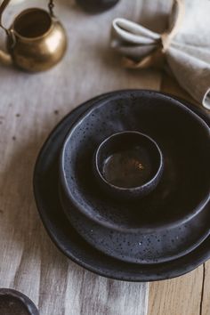 an empty black bowl sitting on top of a wooden table next to two tea kettles