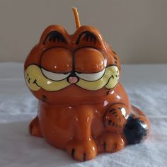 an orange ceramic cat sitting on top of a white sheet with its eyes wide open