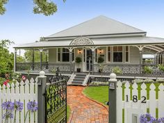 a house with a white picket fence and flowers on the front yard, surrounded by greenery