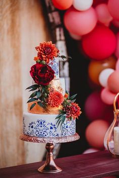 a three tiered cake with flowers on top sitting on a table next to balloons