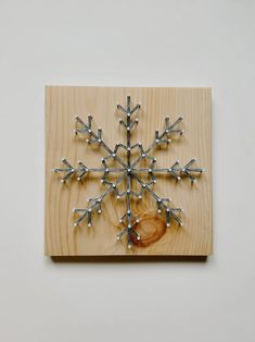 a snowflake is mounted on a wooden plaque with nails and wood shavings