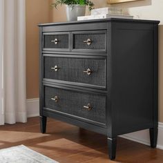 a black dresser with three drawers and a potted plant in the corner on top