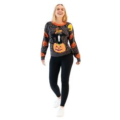 a woman wearing a black and orange sweater with pumpkins on the chest, standing in front of a white background