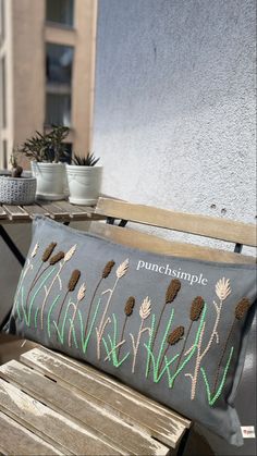 an embroidered pillow sitting on top of a wooden bench next to a potted plant