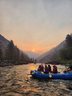 a group of people riding on the back of a raft down a river at sunset