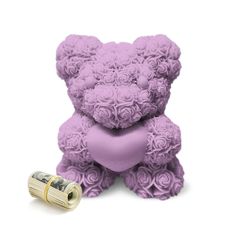 a purple teddy bear sitting next to a roll of money and rolled up roses on the ground