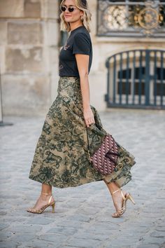 a woman wearing a skirt and heels walking down the street with her hand in her pocket