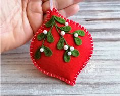 a hand holding a red heart shaped ornament with green leaves and berries on it