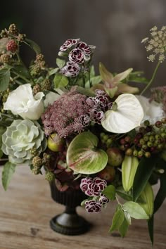 a vase filled with lots of different flowers on top of a wooden table and surrounded by greenery