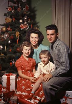 a man and two women sitting next to a little boy in front of a christmas tree