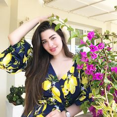 a woman in a blue and yellow dress standing next to purple flowers with her hands on her head