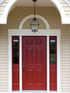 a red front door with two sidelights and a light fixture on the outside of it